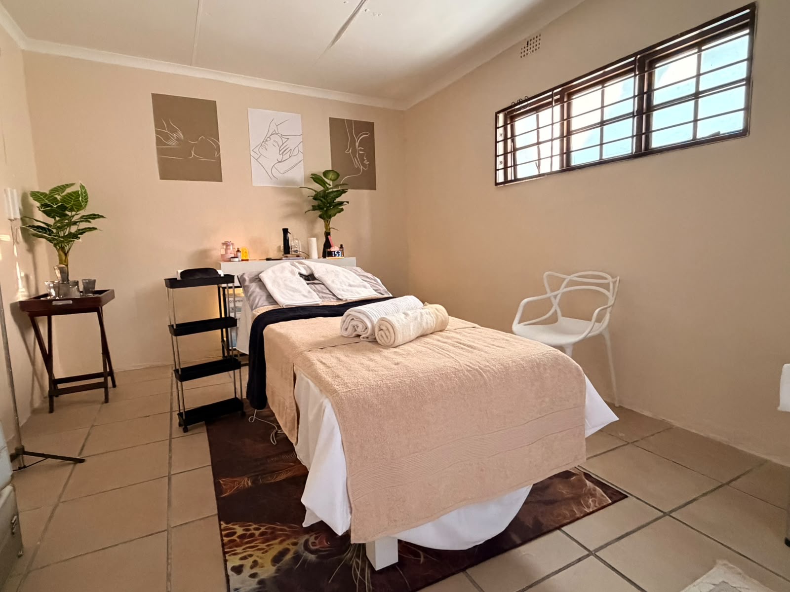 The treatment room with a dressed massage bed, plants and line-art prints